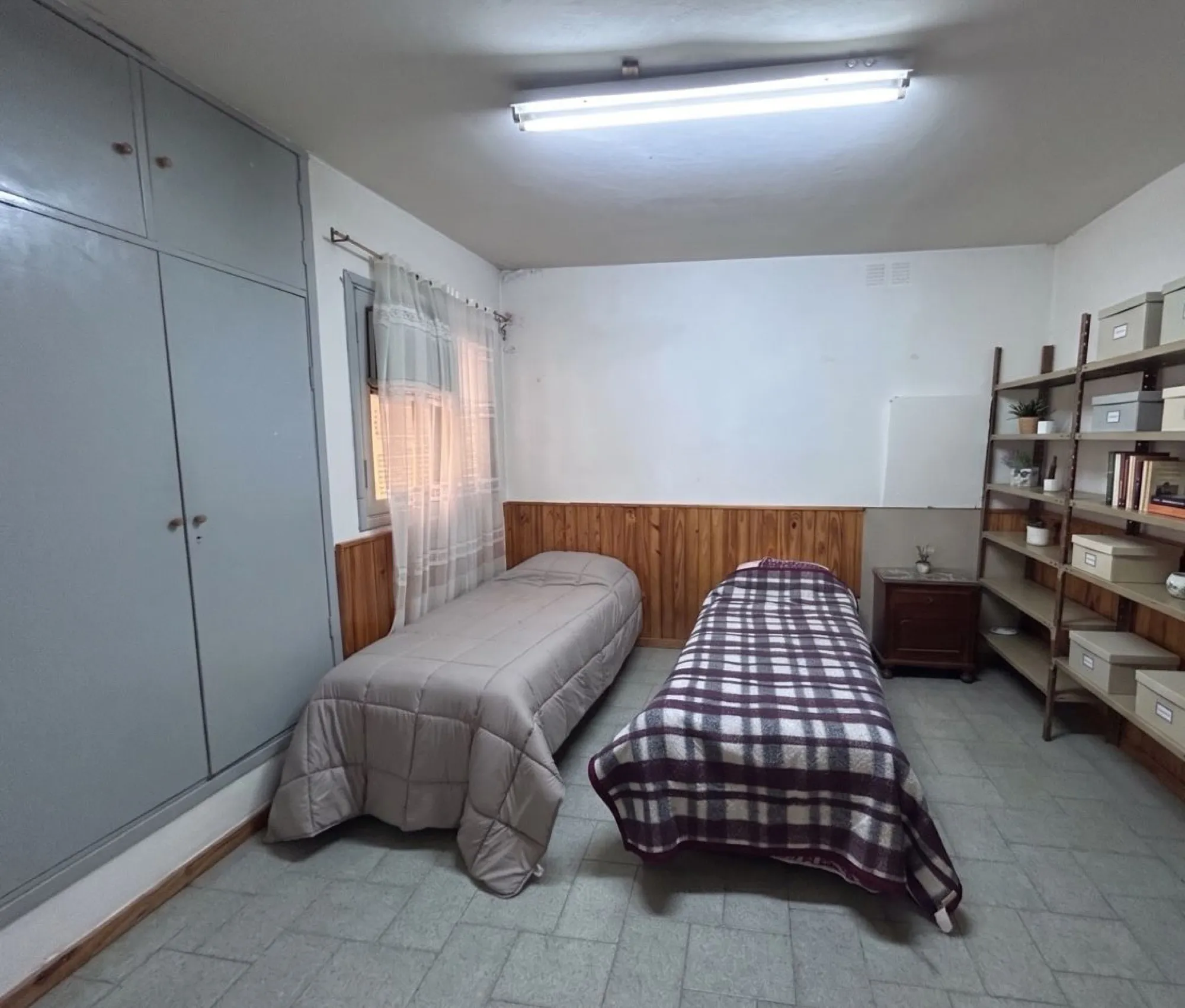 Cuarto con placard gris, dos camas y estantes con cajas.