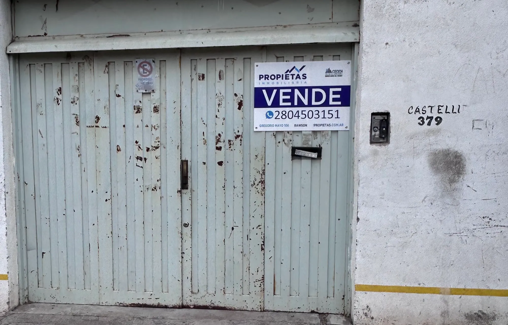 Portón verde del frente sobre calle Castelli, con el cartel de venta de Propietas y el número 379 pintado en la pared.