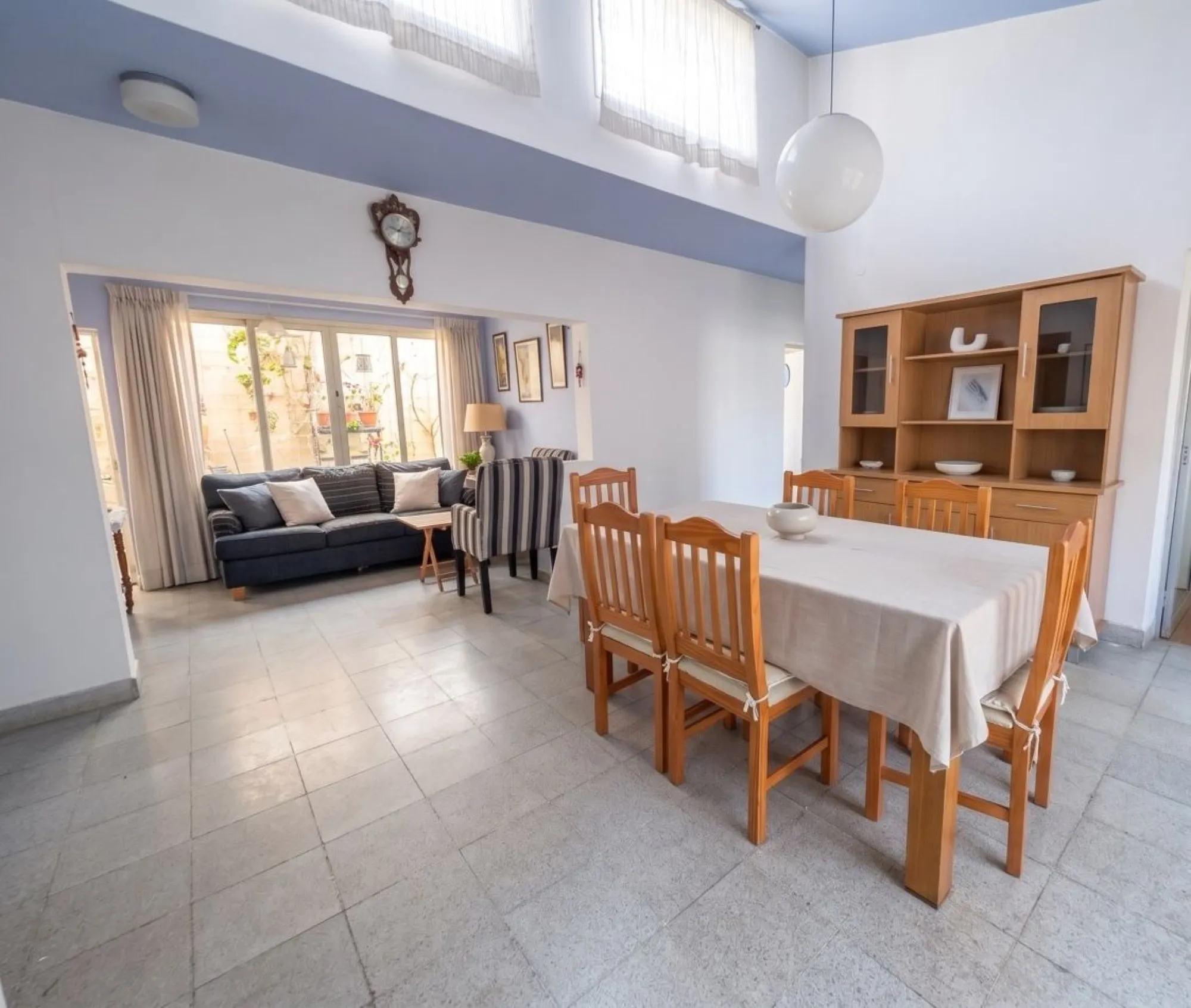 Living comedor de doble altura, con ventanas altas, mesa de madera y aparador.
