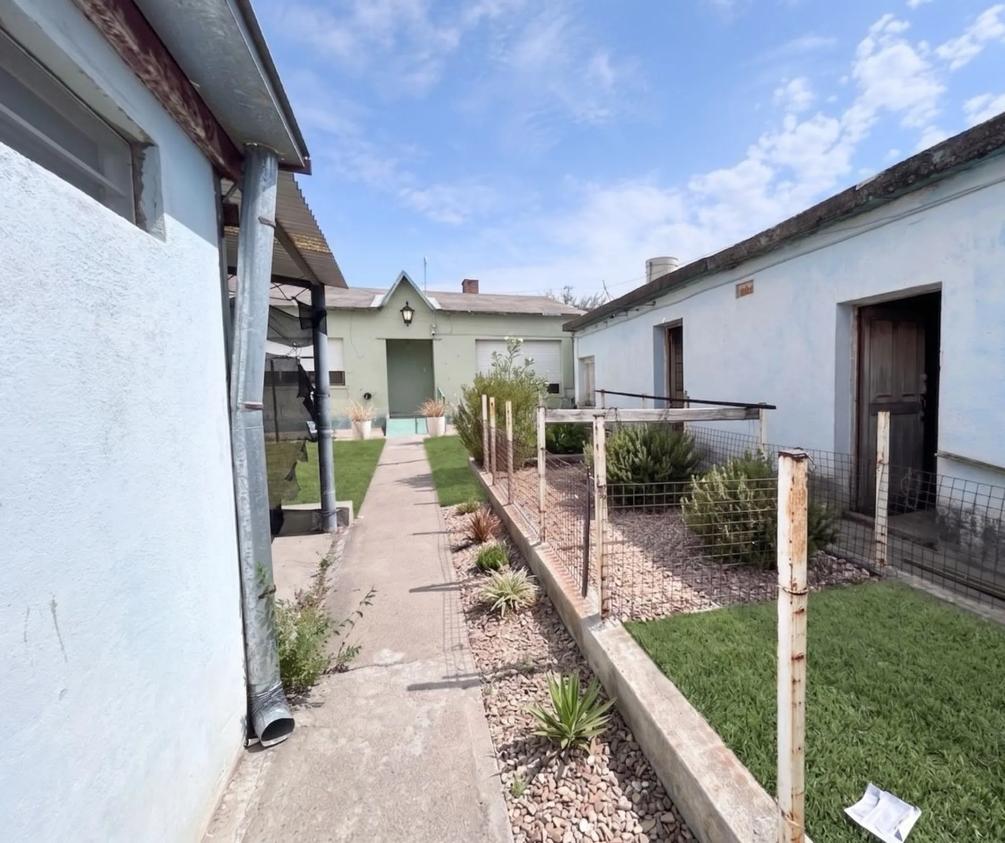 Pasillo de cemento con jardín de piedras al costado, que lleva hacia la casa.