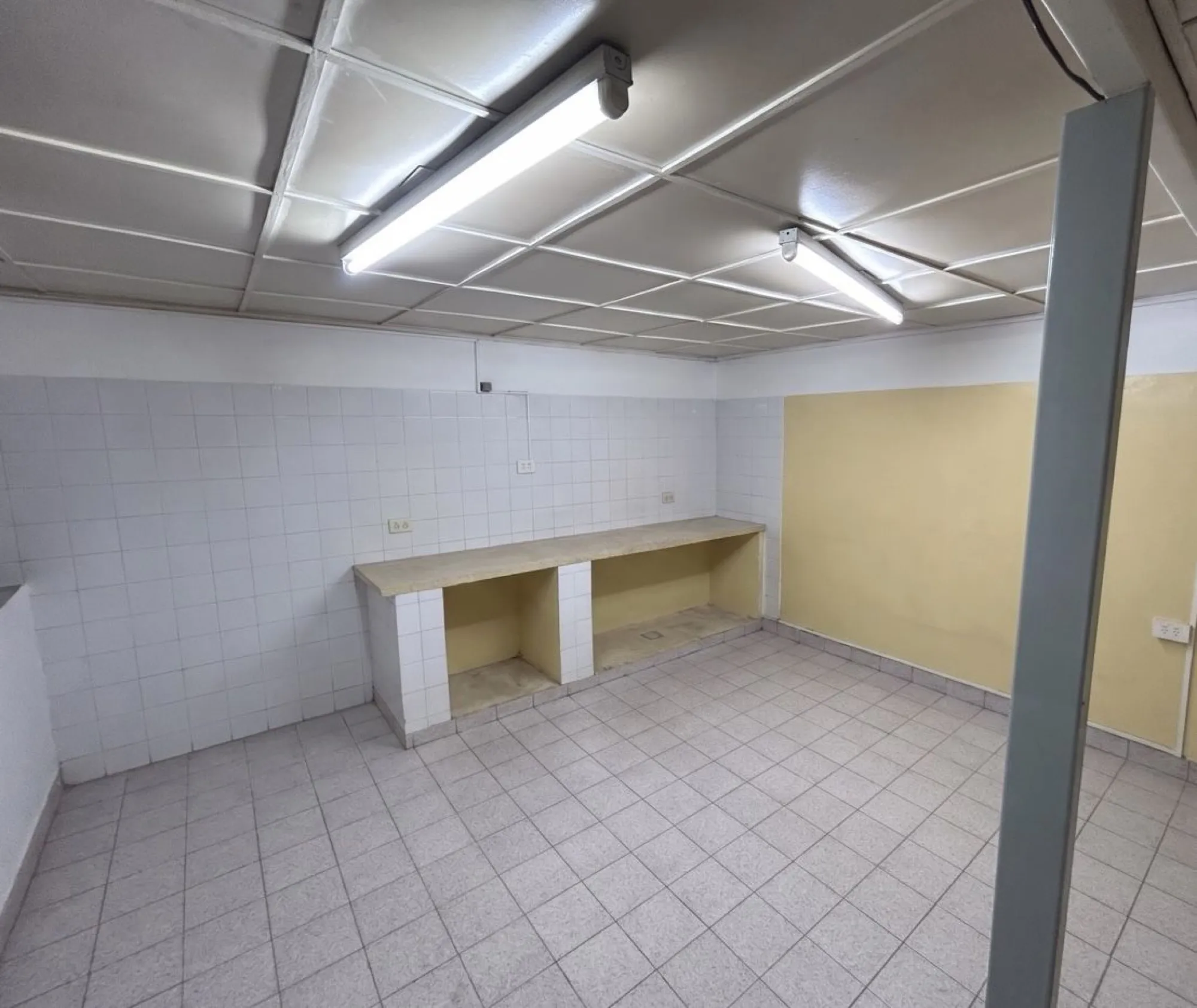 Sala azulejada con una mesada de obra y luces de tubo.